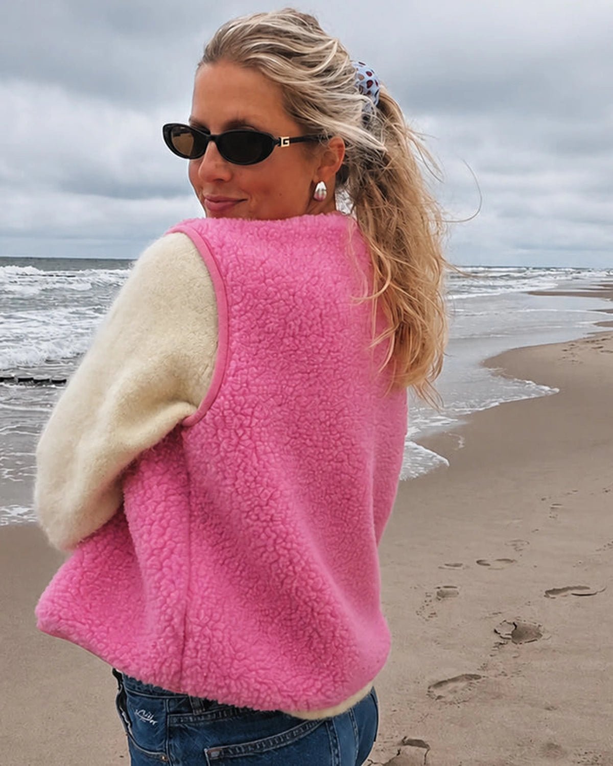 Frau trägt die pinke TYB Wollweste am Strand